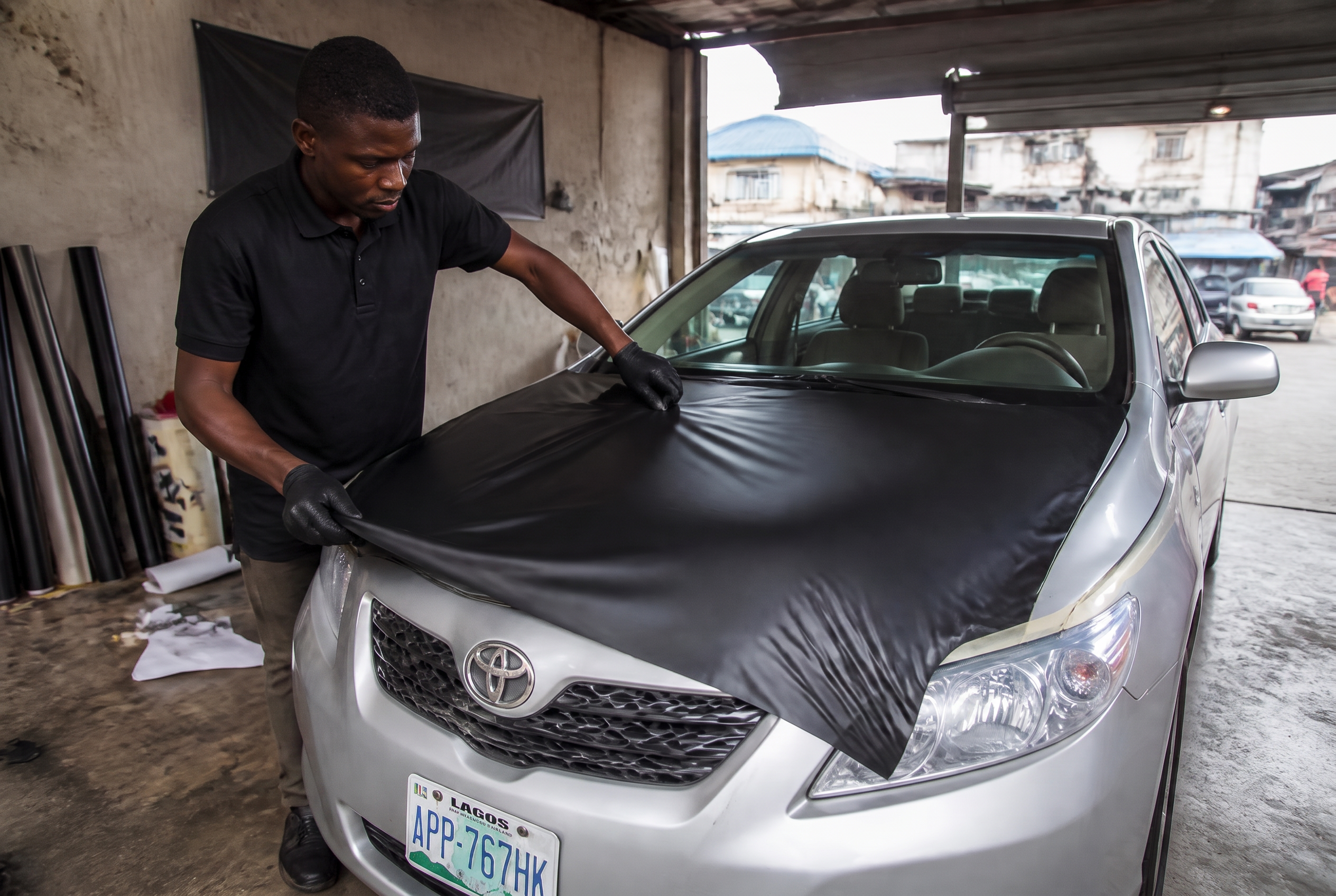 Vehicle wrapping technician applying black film to a Toyota in a workshop in Ibadan